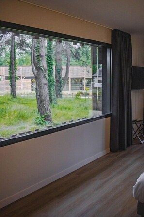 A room with a large window, a flat-screen TV, and a wooden floor. - Hotel La Reposee Rest. L'escu De Runfao (Liffre)