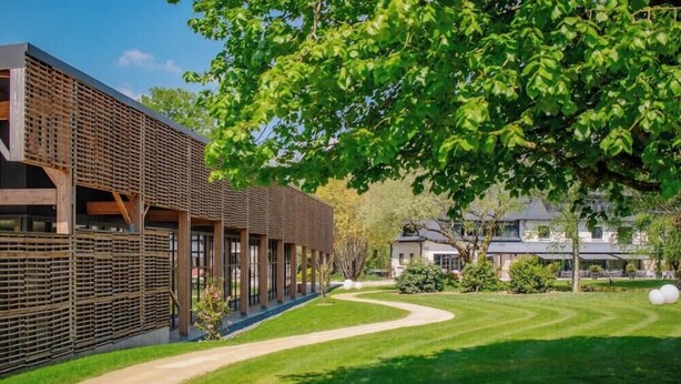 A modern building with a covered walkway, a curved lawn, and a large tree. - Hotel La Reposee Rest. L'escu De Runfao (Liffre)