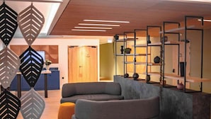 A modern interior with a sectional sofa, a wooden reception desk, and a wall-mounted shelving unit. - Hotel La Reposee Rest. L'escu De Runfao (Liffre)