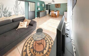 Ein Wohnzimmer mit einer Couch, einem Glastisch, einem Fernseher und einem Essbereich mit Stühlen und einem Tisch.
