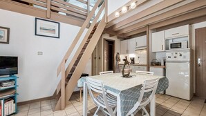 Zona pranzo con tavolo, sedie, una scala, cucina completa di elettrodomestici e televisione.