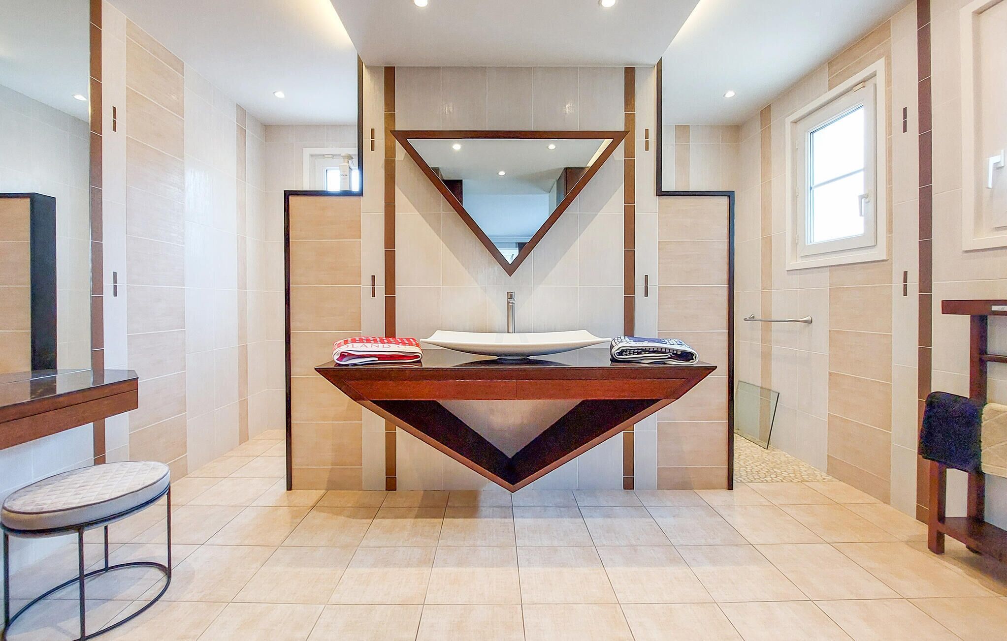 A modern bathroom with a unique triangular sink, a mirror, and a small stool.