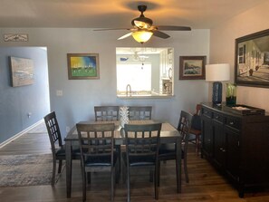 A dining area with a ceiling fan, a window with a view, and a painting on the wall.