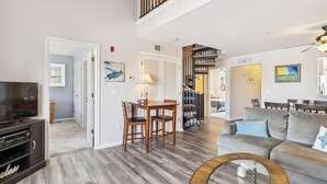 Un salon avec un téléviseur, un coin repas avec des chaises, un escalier et un canapé.