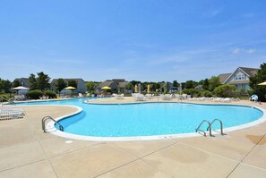 Une piscine entourée de maisons, avec des chaises longues et des parasols.
