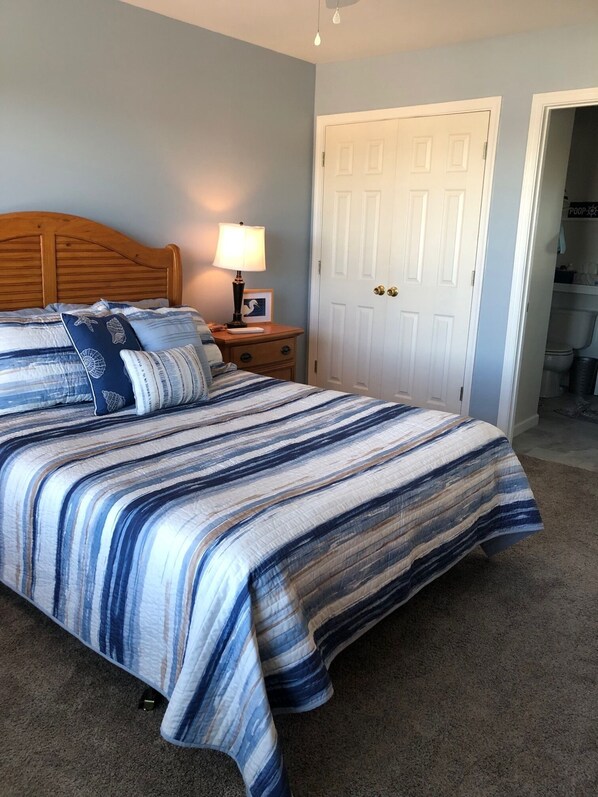 Quarto com cama, mesa de cabeceira, luminária e porta para o banheiro.