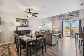 A spacious living area with a dining table, chairs, a sofa, and a balcony with a view.