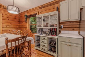 A wooden cabin interior with a dining table, chairs, a coffee station, and a cabinet. - Smoky Mountain Cabin: King Bed, Hot Tub, Zero Pet Fees, 15 Minutes to Train (Whittier)