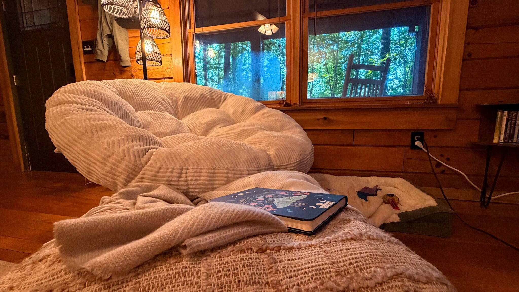 Una habitación acogedora con un sillón informal, una manta y un libro sobre una alfombra pequeña.