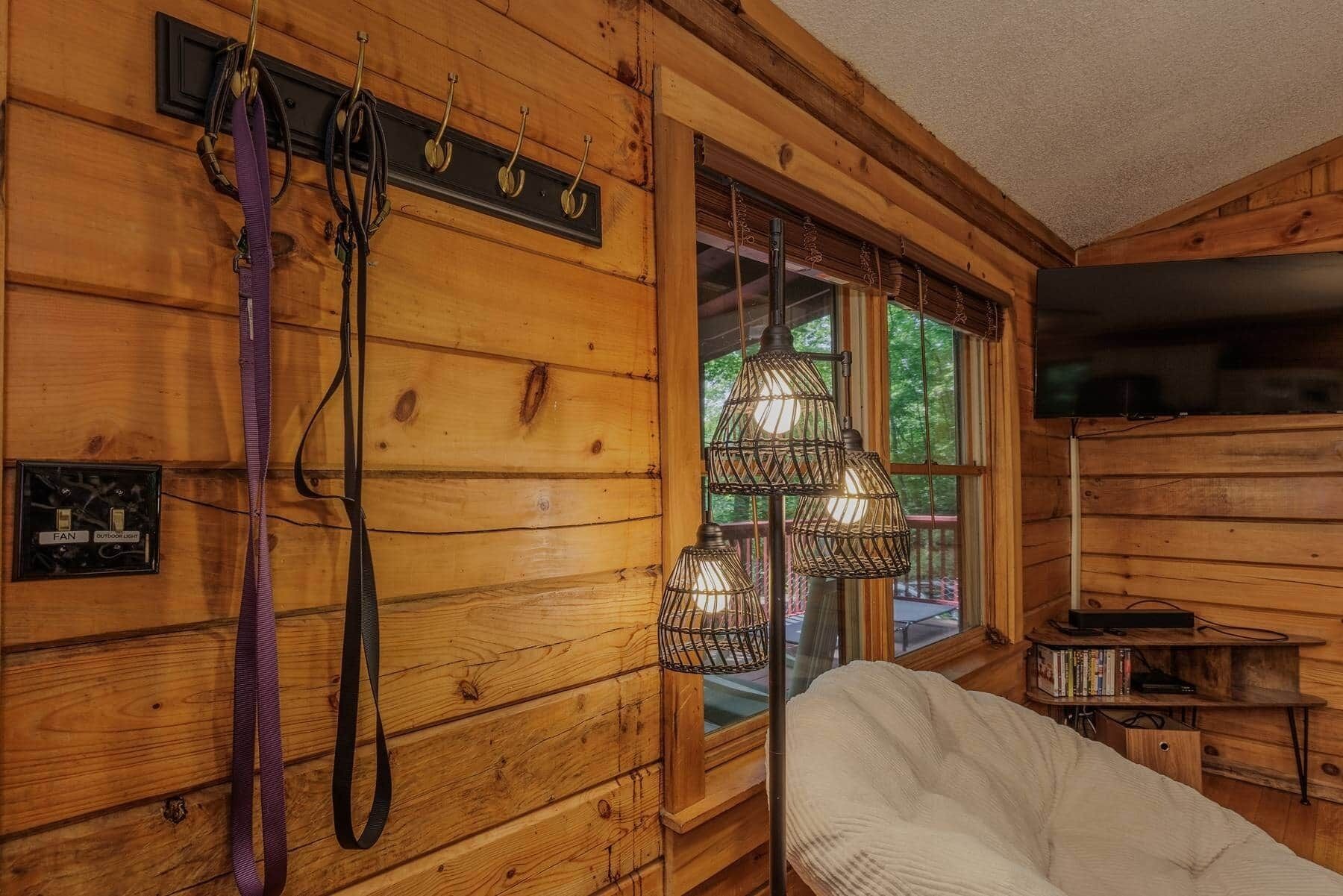 A wooden cabin interior with a white chair, a window with a view, and a mounted television.