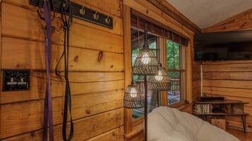 A wooden cabin interior with a white chair, a window with a view, and a mounted television.