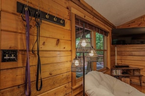 A wooden cabin interior with a white chair, a window with a view, and a mounted television. - Smoky Mountain Cabin: King Bed, Hot Tub, Zero Pet Fees, 15 Minutes to Train (Whittier)
