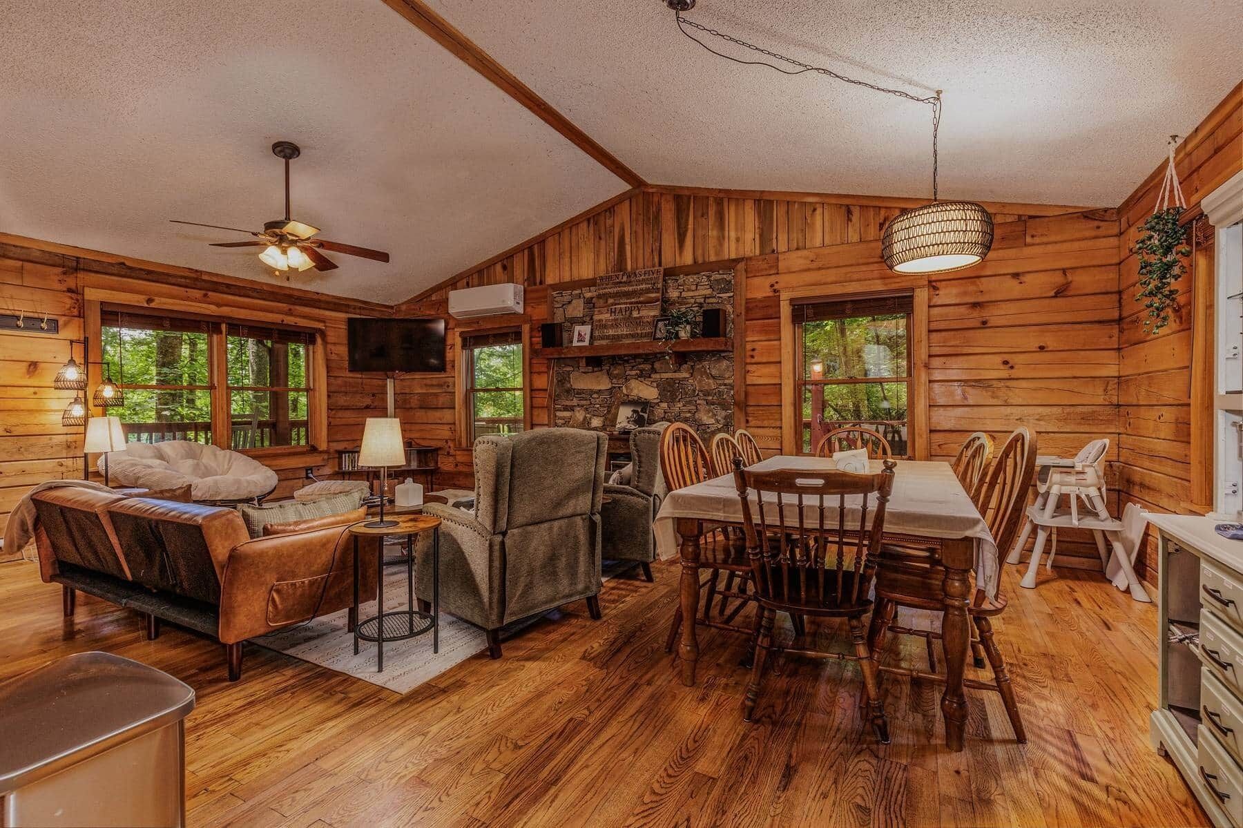 A log cabin interior with a dining area, seating, a television, and a stone wall.