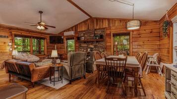 A log cabin interior with a dining area, seating, a television, and a stone wall.
