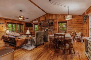 Ein Holzblockhaus-Interieur mit Essbereich, Sitzmöglichkeiten, Fernseher und einer Steinwand.