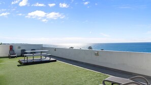 A rooftop terrace with a view of the sea, a table, chairs, and a small garden area. - Water View Coastal Loft in Manly Pool Access (Manly)