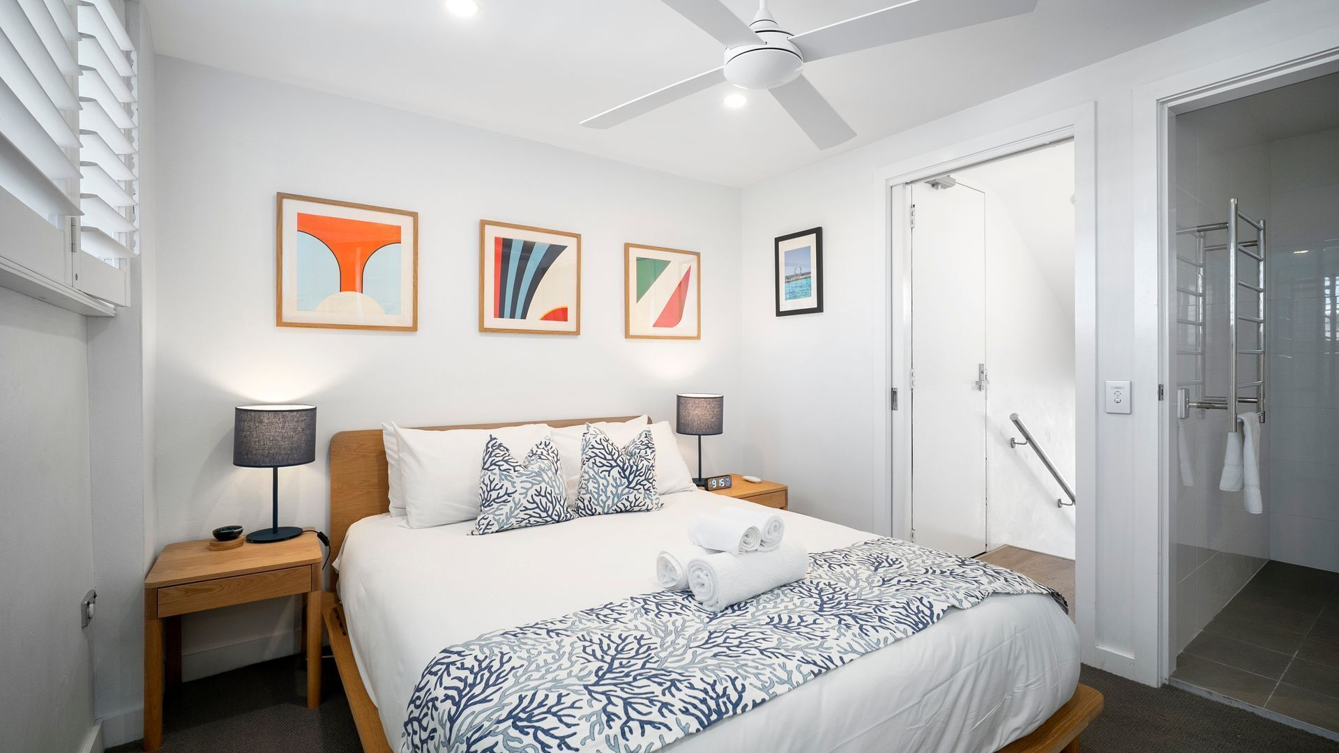 Ein modernes Hotelzimmer mit einem Bett, zwei Nachttischen, einem Deckenventilator und Kunstwerken an der Wand.