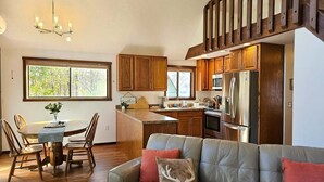 A modern kitchen with wooden cabinets, a stainless steel refrigerator, and a dining area with a table and chairs.