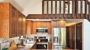 A kitchen with wooden cabinets, stainless steel appliances, and a wooden staircase.