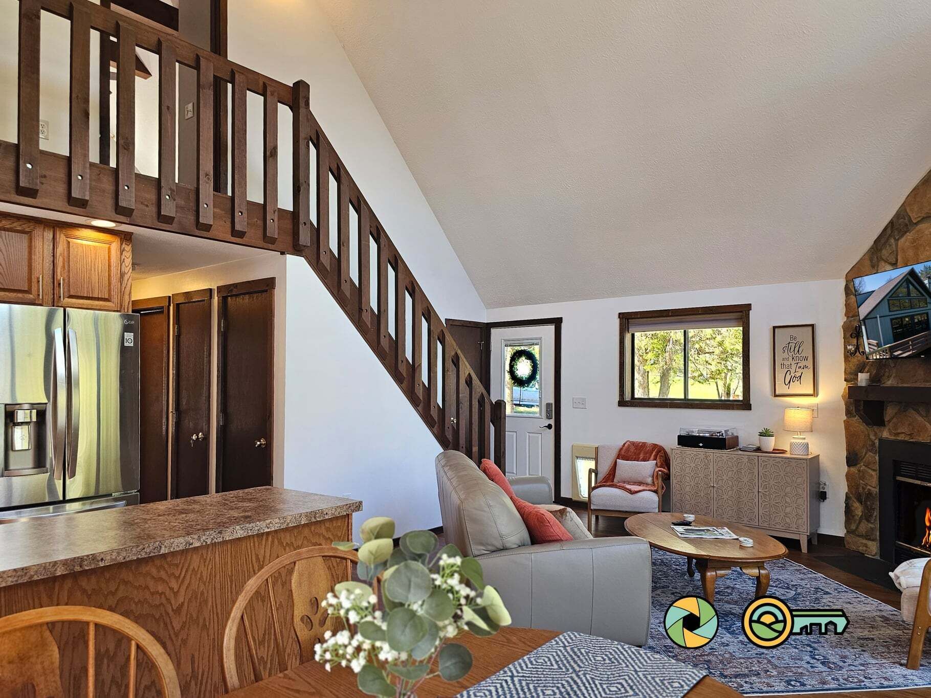 Un vaste espace de vie agrémenté d’un escalier en bois, une cuisine équipée d’un réfrigérateur, une cheminée et un coin repas avec une table et des chaises.