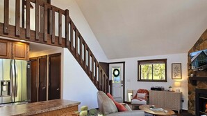 A spacious living area with a wooden staircase, a kitchen with a refrigerator, a fireplace, and a dining area with a table and chairs.