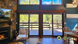 A room with a stone fireplace, a large sliding glass door leading to an outdoor deck, a television, and a dining area.