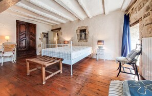 Ein Schlafzimmer mit Holzboden, Metallbettgestell, einer Holzbank, einem Stuhl, einem kleinen Nachttisch und einem Kleiderschrank.