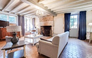 Ein Wohnzimmer mit Kamin, einer Couch, einem Tisch mit einer Vase und einer Deckenleuchte.