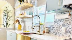 Una cocina con salpicadero estampado, un lavamanos de acero inoxidable, una estufa blanca y un suelo amarillo con diseño.