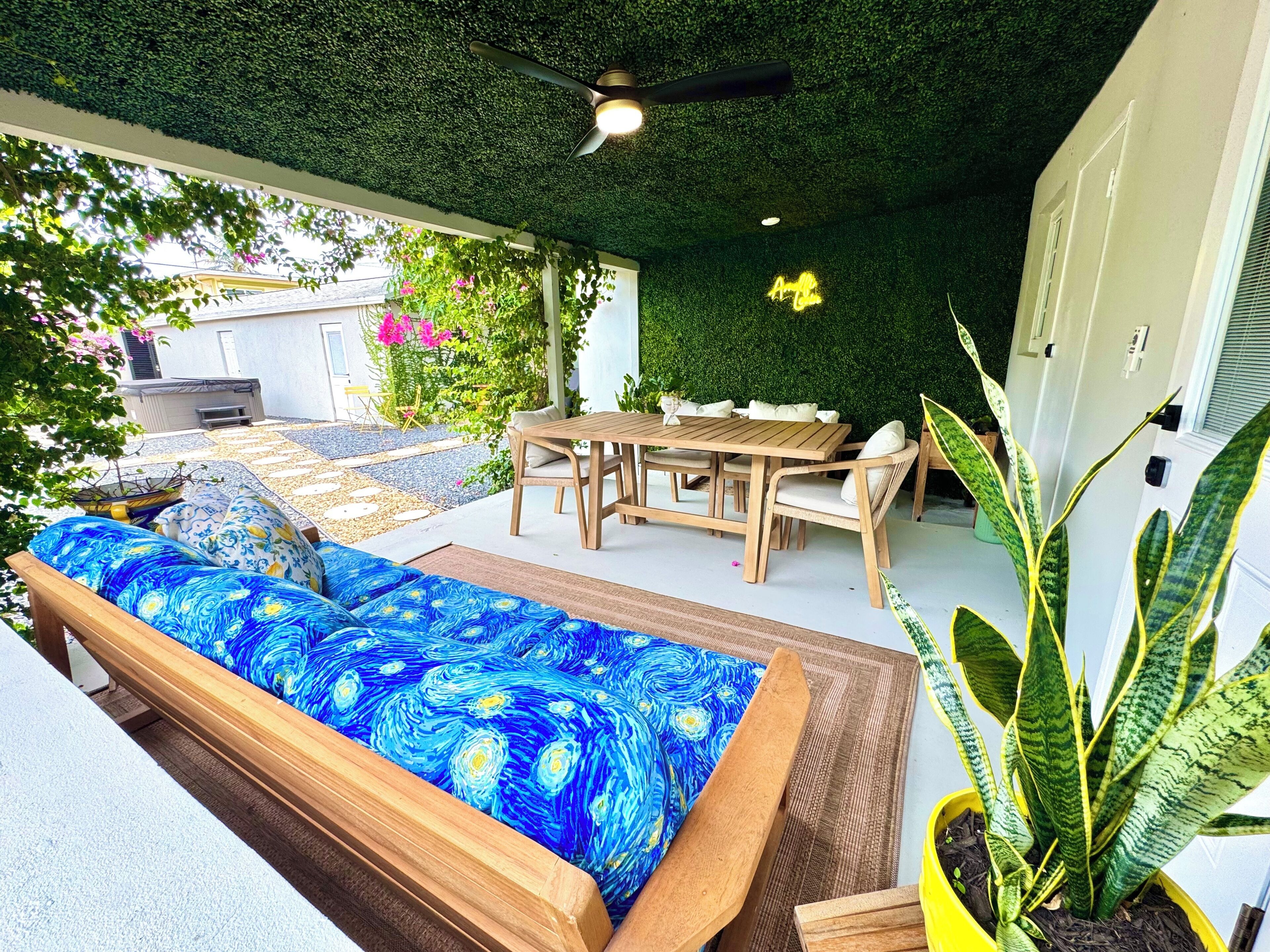 An outdoor seating area with a wooden table and chairs, a sofa with a blue patterned cover, and a potted plant.