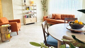 Una sala de estar con sofá, sillón, mesa de comedor y una planta.