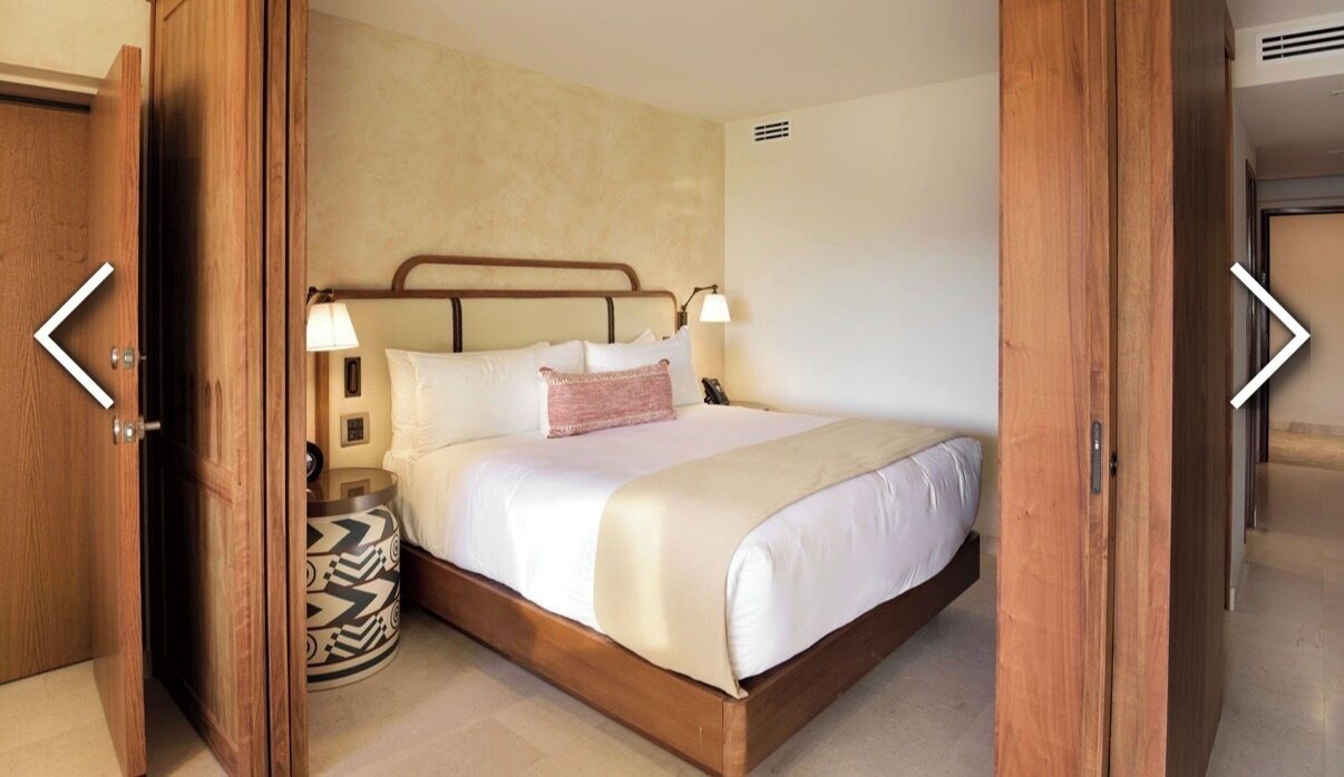 Une chambre d’hôtel avec un lit en bois, une lampe de chevet, une table de chevet et un tapis à motifs.
