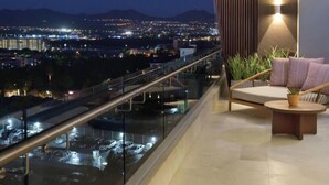 Un balcon donnant sur une vue de la ville la nuit, un canapé et une petite table avec une plante.
