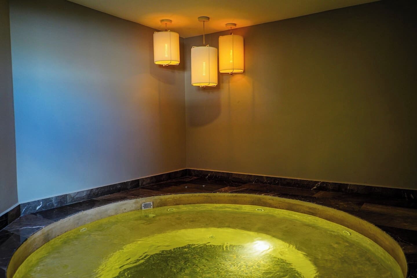 Un espace spa comprenant un jacuzzi, un sol en marbre et des luminaires fixés au mur.