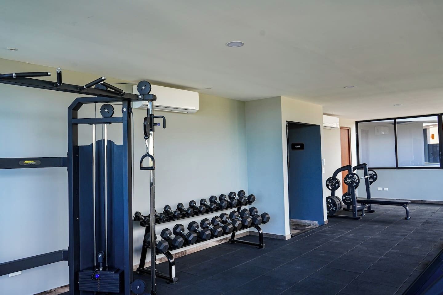 A gym with weightlifting equipment, dumbbells, and a bench.