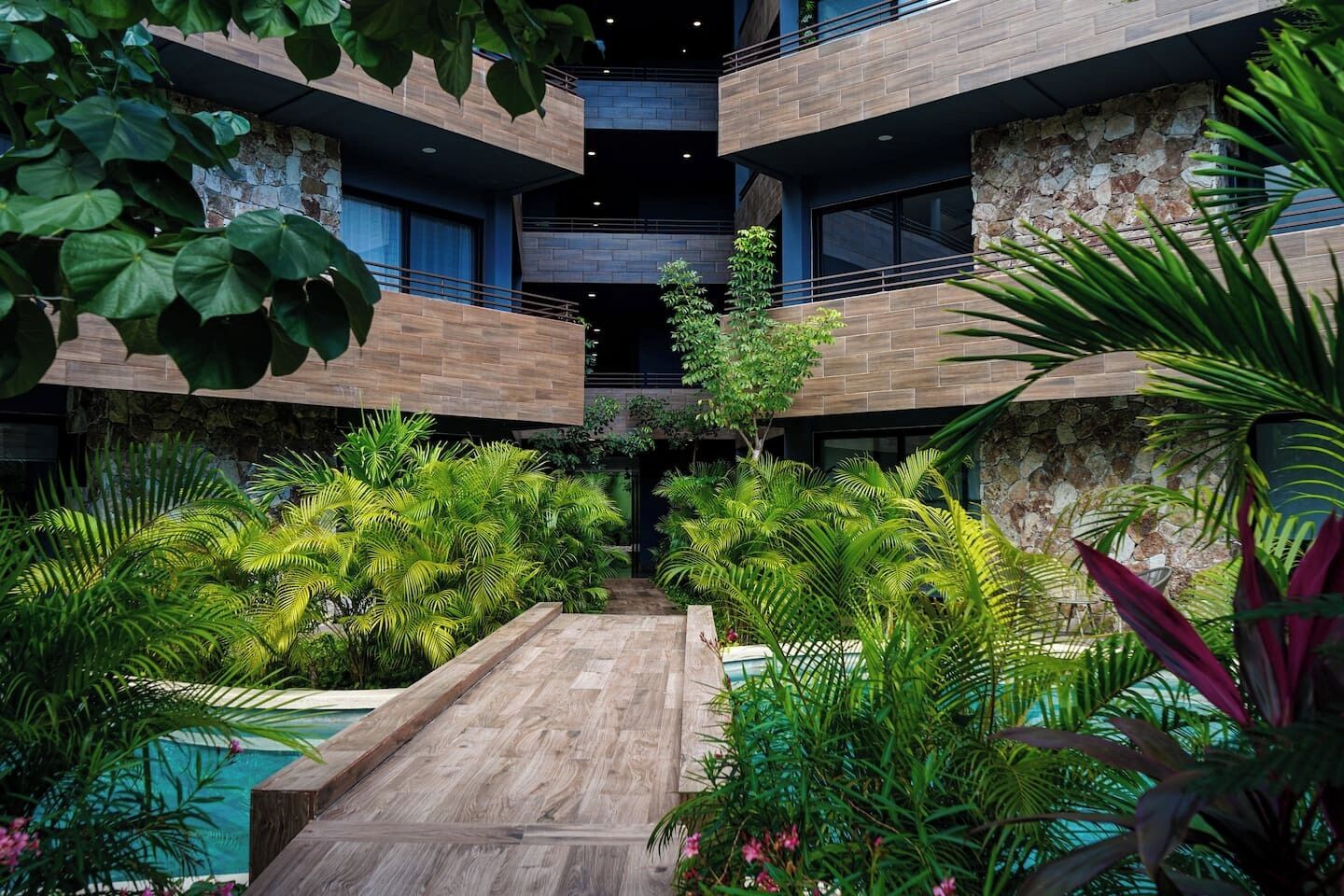Un immeuble à plusieurs niveaux doté d’un atrium central, entouré d’une végétation luxuriante et d’une terrasse en bois.