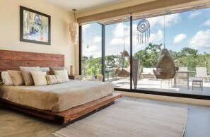 Ein Schlafzimmer mit einem großen Bett, Blick ins Freie und einem Hängekorbsessel.