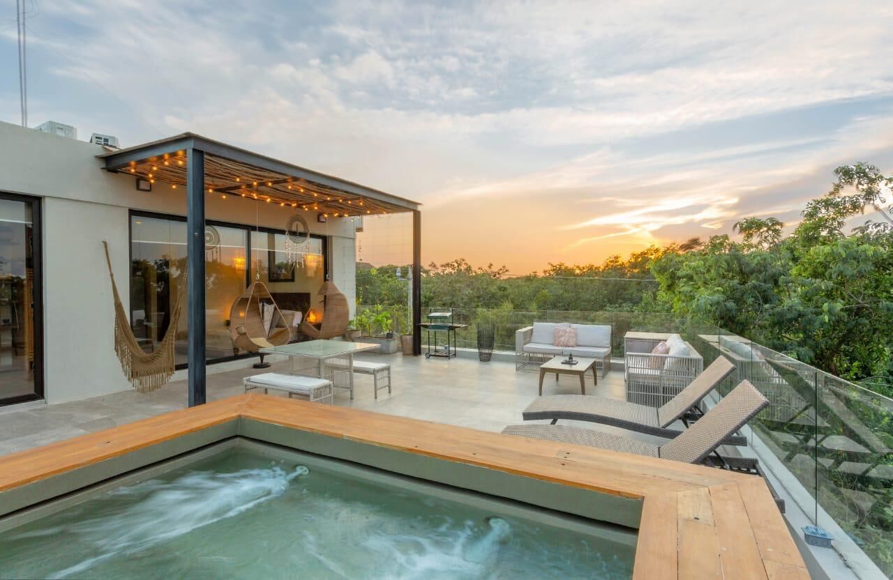 A modern outdoor living space with a hot tub, seating area, and glass doors leading to an interior.