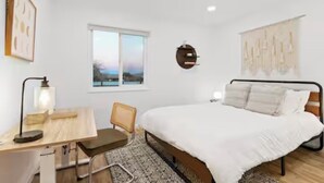 A bedroom with a bed, a desk, a chair, a window, and a wall art piece. - Desert Rose Retreat (Joshua Tree)