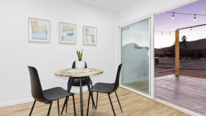 A modern interior with a dining area, a potted plant, and a large sliding glass door leading to an outdoor deck. - Desert Rose Retreat (Joshua Tree)