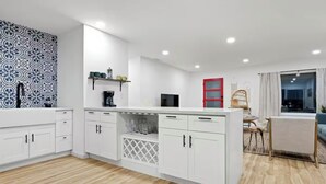 A modern kitchen with white cabinetry, a built-in wine cooler, and a red-framed door. - Desert Rose Retreat (Joshua Tree)