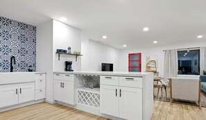 A modern kitchen with white cabinetry, a built-in wine cooler, and a red-framed door. - Desert Rose Retreat (Joshua Tree)