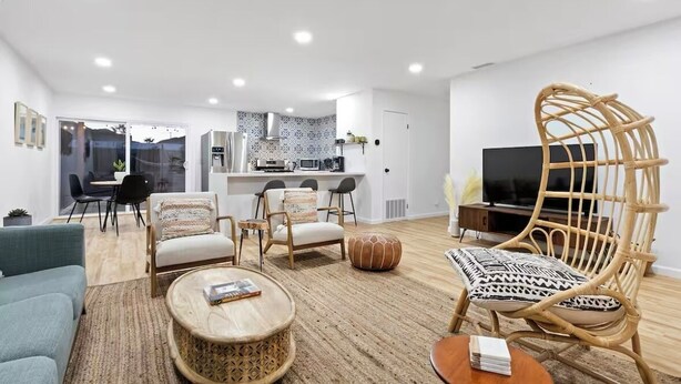 A modern living room with a sofa, coffee table, wicker chairs, and a television. - Desert Rose Retreat (Joshua Tree)