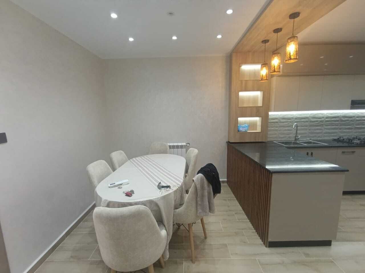 Una cocina moderna con una isla integrada, un comedor con mesa redonda y sillas, e iluminación empotrada en el techo.