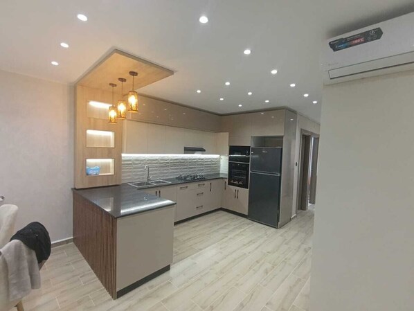 A modern kitchen with a central island, built-in appliances, and recessed ceiling lighting. - Résidence Oasis (Filfila)