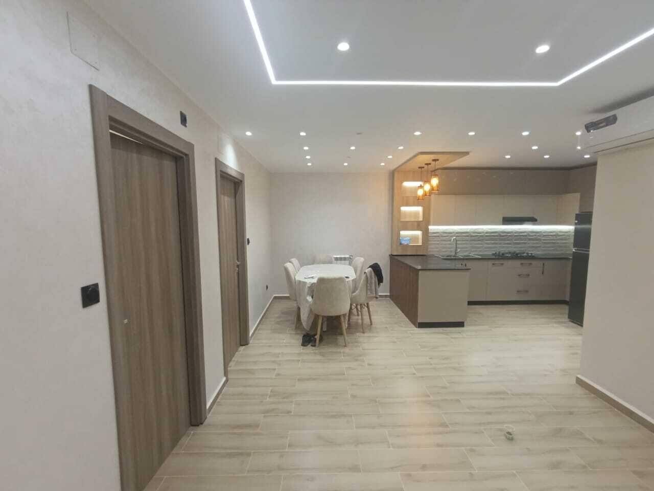 A modern kitchen with a central island, a dining area with a table and chairs, and a hallway with doors.