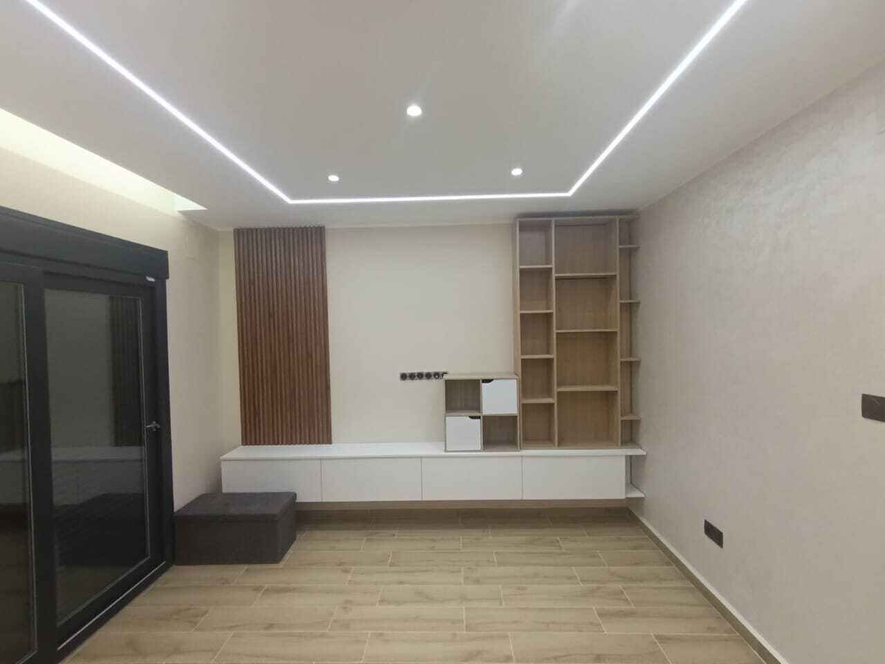A modern room with a built-in bench, recessed ceiling lighting, and a wooden floor.