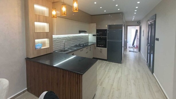 A modern kitchen with a central island, built-in appliances, and pendant lighting. - Résidence Oasis (Filfila)