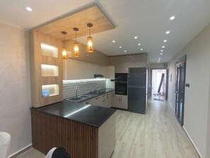 A modern kitchen with a central island, built-in appliances, and pendant lighting. - Résidence Oasis (Filfila)