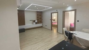 A spacious room with a wooden floor, a dining table, and a built-in shelving unit. - Résidence Oasis (Filfila)